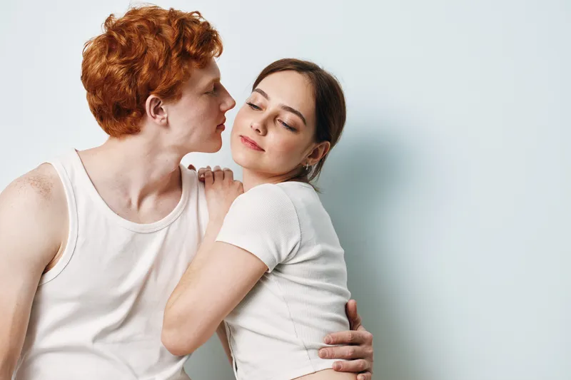 Couple, young man and woman embracing with closed eyes in white clothes, close intimacy and affection with romantic mood on light background for love and connection.