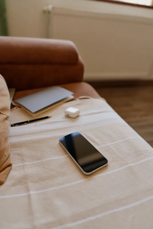Cozy home scene with a phone on a striped table, a notebook and pen nearby, soft natural light, relaxed workspace mood, everyday living atmosphere