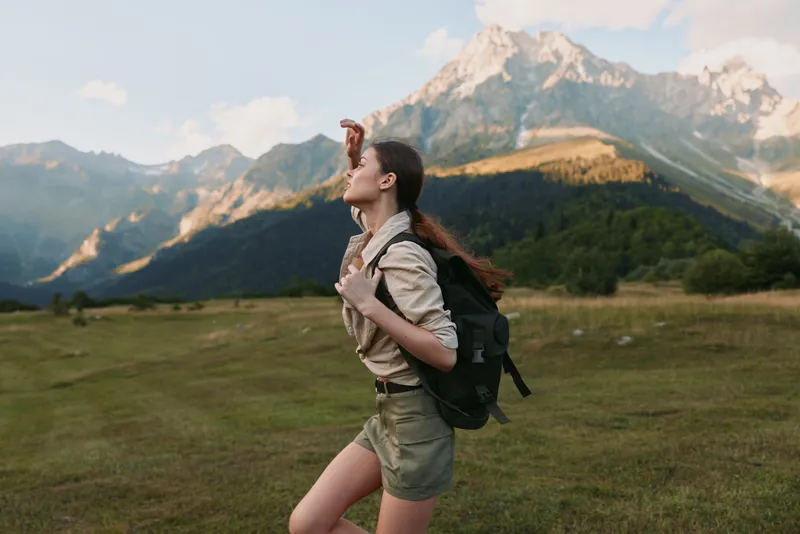 Active woman hiking in mountains with a backpack, running across a grassy meadow. Bright nature scenery conveys adventure, wellness, and outdoor lifestyle. Joyful energy.