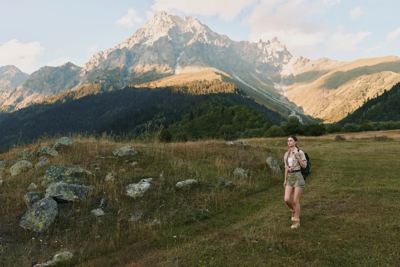 Young woman hiking in mountains, carrying backpack, enjoying nature, sunny day, casual outfit, scenic landscape, outdoor lifestyle, adventure, freedom