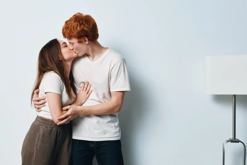 Couple kissing and hugging on light background for love, relationship, romance and intimacy between young people with affection, tenderness and connection at home.