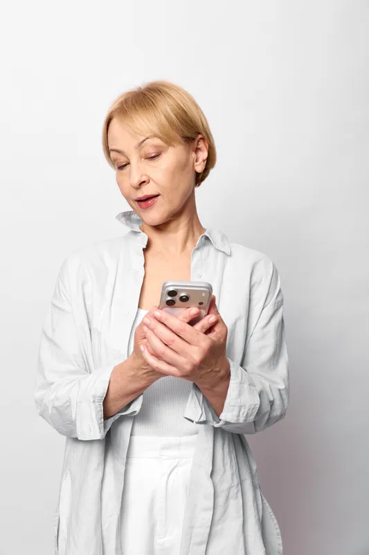 Woman smartphone messaging technology stress anxiety communication surprised portrait on white background. Blonde woman in casual shirt frowns at phone screen, concept for digital stress.