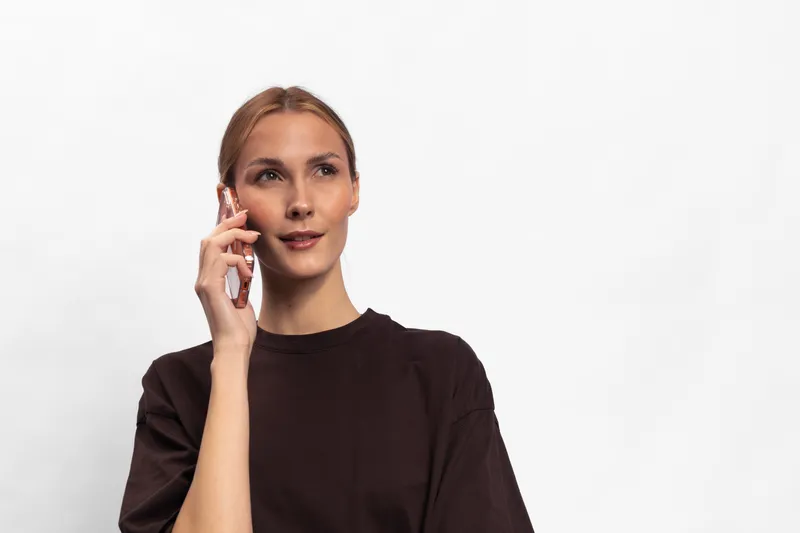 Young woman in dark shirt talks on smartphone with thoughtful expression. Isolated on white background. Concept for communication, technology, connection, and modern lifestyle.