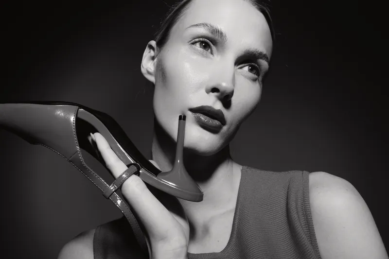 Portrait of a fair skinned caucasian woman holding a high heel shoe near her face in black and white.