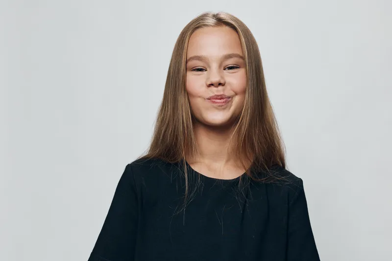 Girl with long hair wearing black shirt smiling and posing on white background, happy facial expression and casual style for portrait or lifestyle image.