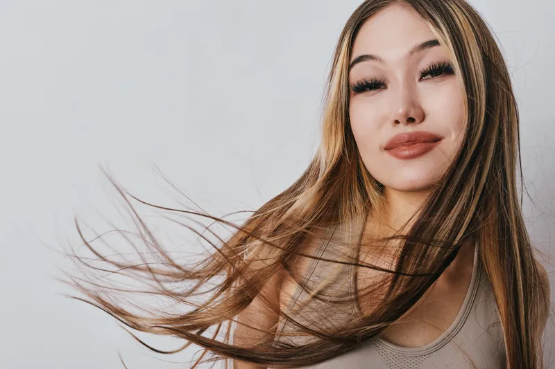 Woman with long hair and natural makeup posing with confident expression against white background. Closeup portrait of female model with smooth skin and loose brown hair.