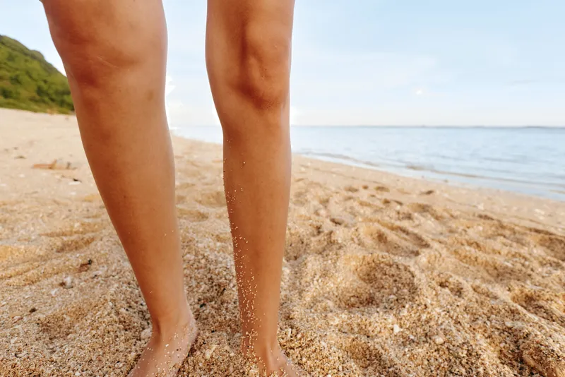 Beach sand ocean shoreline, barefoot legs walking on warm beach, summer travel relaxation mood, golden light, close up of lower body, natural outdoor scene, near calm sea waves, footprints