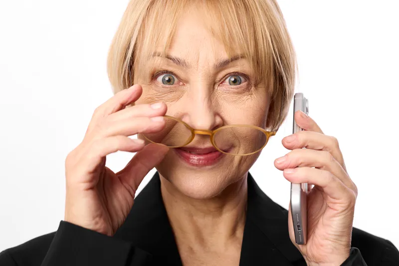 Senior woman smiling, holding eyeglasses and adjusting frames with both hands, close up studio portrait on white background, concept vision care and eye health.