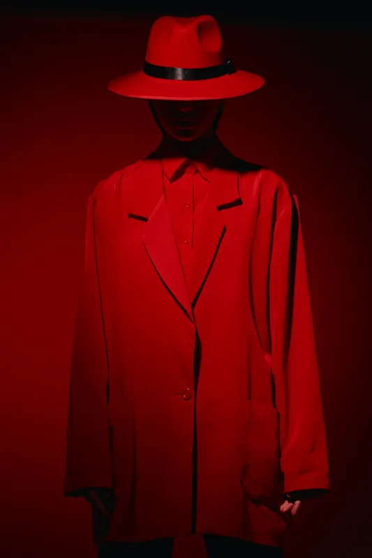 Fashion model dressed in oversized red suit and matching hat posed in low red light, creating dramatic shadows. Concept for beauty, creativity, and bold fashion statements.