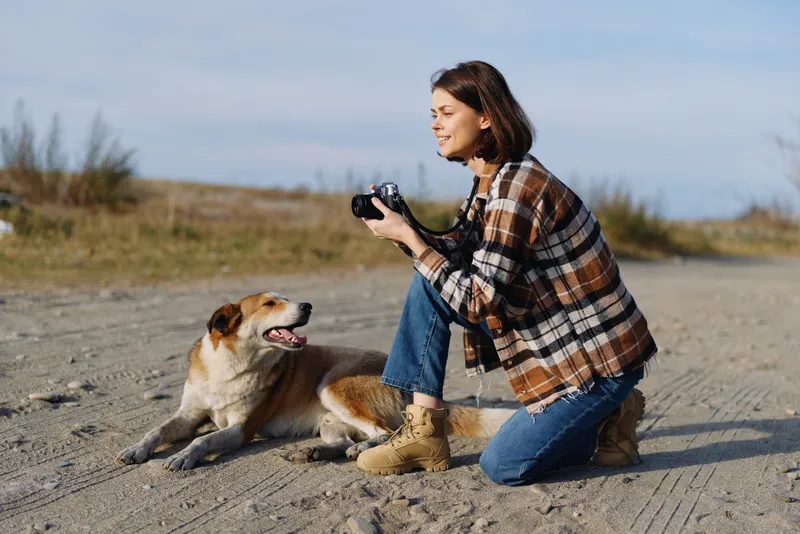 Photography outdoor woman dog camera sand desert companionship landscape nature casual clothing boots plaid jacket moment scene with lens in hand and calm horizon under bright light