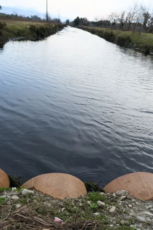 River water flows through a rural landscape, bordered by stones and round rocks. Outdoor nature view with calm ripples under overcast light, a peaceful lifestyle for relaxation.