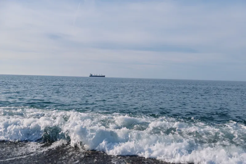 Sea and ocean view with rolling waves near a rocky shore, distant ship on the horizon, calm blue water and open sky, maritime scenery perfect for travel, nature, or coastal lifestyle