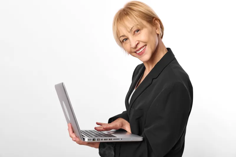 Businesswoman, laptop, smile, studio portrait, smiling senior woman in black suit holding notebook, confident professional, soft light on white background, focused eyes, modern technology, relaxed