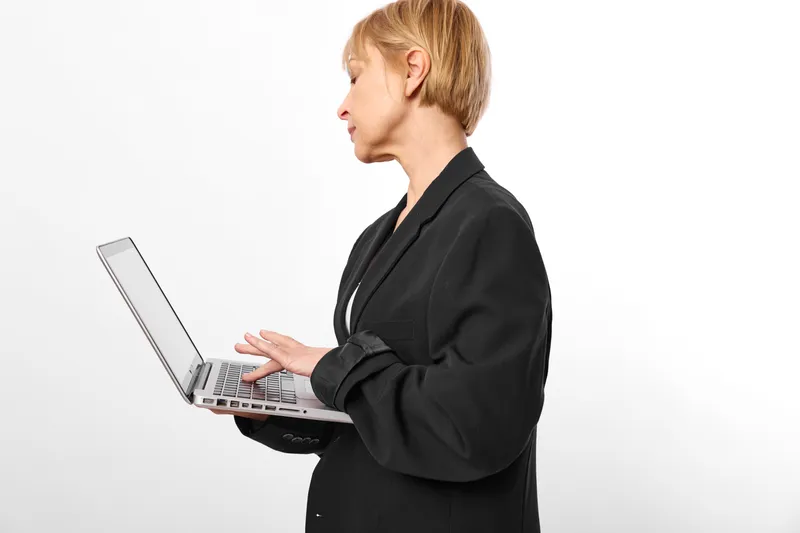 Woman with short blond hair works on laptop in office, typing on keyboard in profile, professional communication with technology, studio white background.