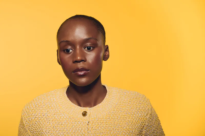 Portrait of a serious dark skinned African woman wearing a yellow knitted sweater on a yellow background. Concept of fashion, beauty, and natural skin tone in studio lighting.
