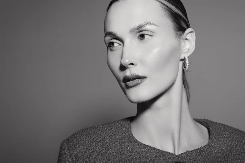 Portrait of a pale white woman with slicked hair and earrings looking sideways in black and white. Concept of elegance and fashion.