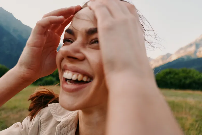 Candid woman lifestyle portrait outdoors with mountains in the background, smiling and cheerful, close up of a happy face, natural light and joyful moment in nature