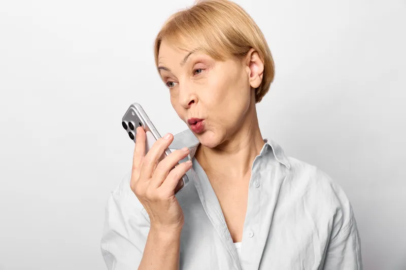 Woman using smartphone with surprise expression, close portrait, studio background light gray, communication and mobile technology concept, soft neutral lighting, calm