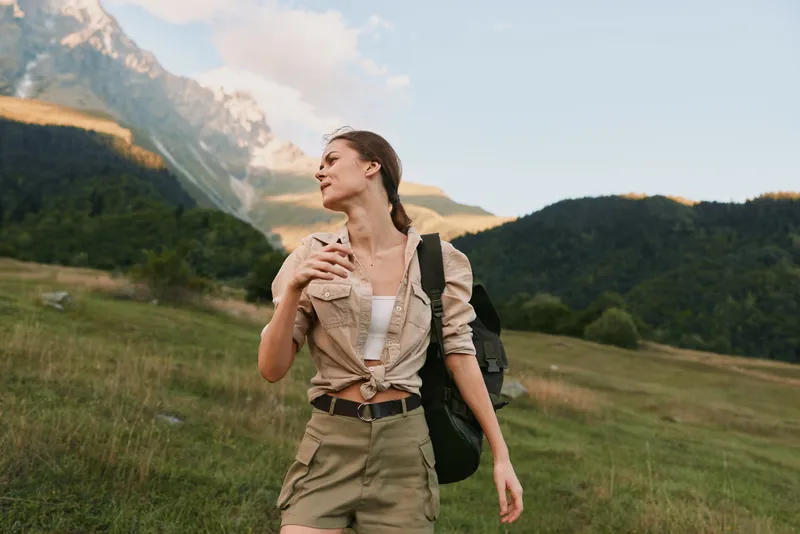 woman hiker in outdoor landscape stands in a grassy valley with mountains in the distance, backpack ready, capturing a moment of nature and adventure