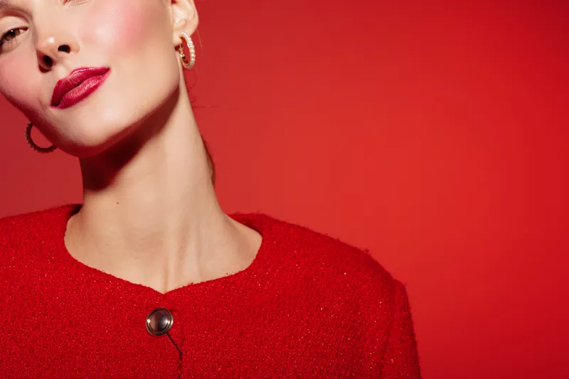 Close-up of elegant woman with red lipstick and red sweater on red background. Fashion portrait with minimalistic style and confident expression. Concept of beauty, style, and glamour.