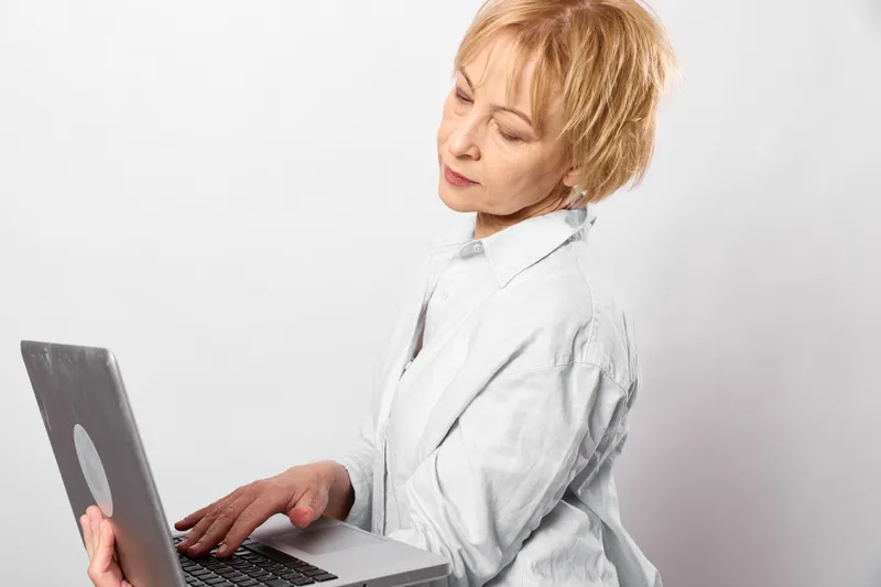 Woman laptop typing office tired burnout side view white background technology focus anxious mood quiet workspace natural light sleepy headache stress respiratory discomfort