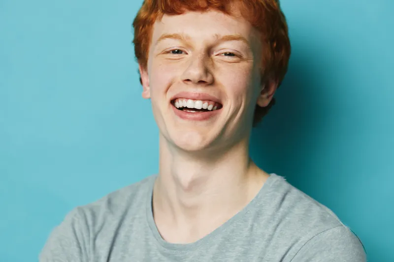 Redhead man smiling with teeth showing in casual shirt against blue background for positive emotion happiness and youth portrait lifestyle.