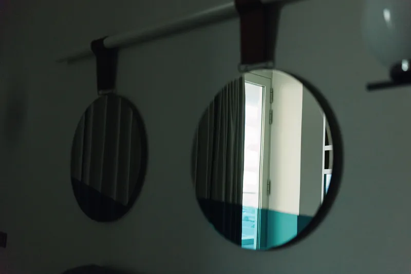 Round mirrors on a dim wall reflect a bright doorway and blue accents, creating a moody interior reflection and architectural atmosphere.