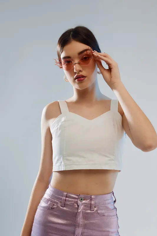 Young woman with beauty and fashion style wears pink sunglasses and white crop top. She poses confidently against a plain background. Concept of modern fashion and elegance.