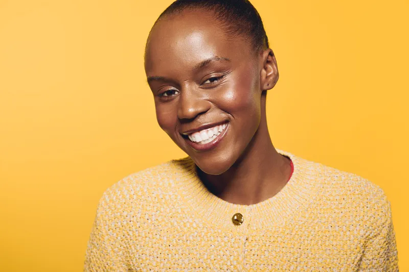 Happy African woman with dark skin smiles warmly wearing a yellow sweater against a yellow background. Concept of joy, natural beauty, and positive emotions in studio portrait.