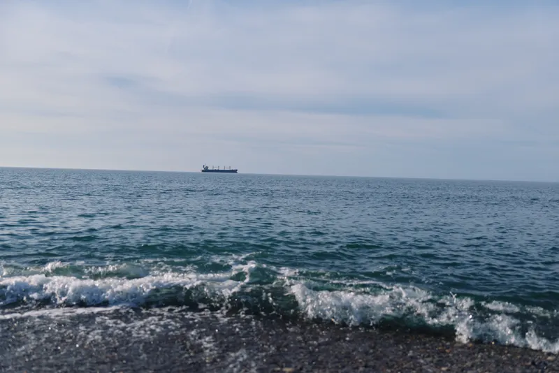 Calm seascape with a distant ship on the horizon, gentle waves breaking on the rocky shore, and a clear sky. Serene maritime mood suited for travel, nature, and landscape stock photography, ideal for