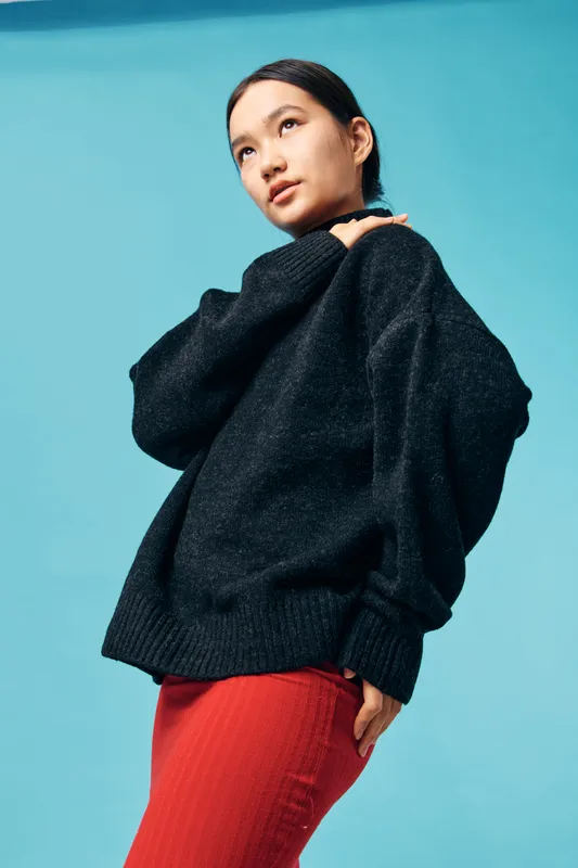 Young woman in black sweater and red skirt posing thoughtful on blue background. Fashion, casual style and confident expression with minimal makeup and tied hair for portrait.