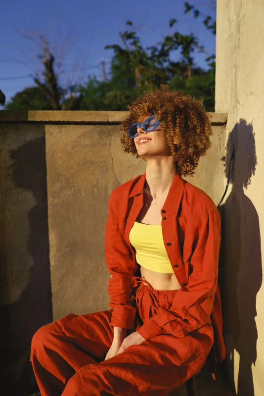 Woman outdoors in a bright orange suit and yellow crop top, cheerful and relaxed, showcasing lifestyle fashion with sunny, vibrant colors and casual, stylish mood and energy