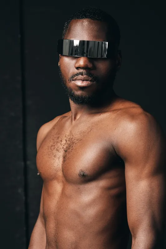 African man with muscular body and beard wearing futuristic visor glasses in creative conceptual visual style with dark background and strong lighting.