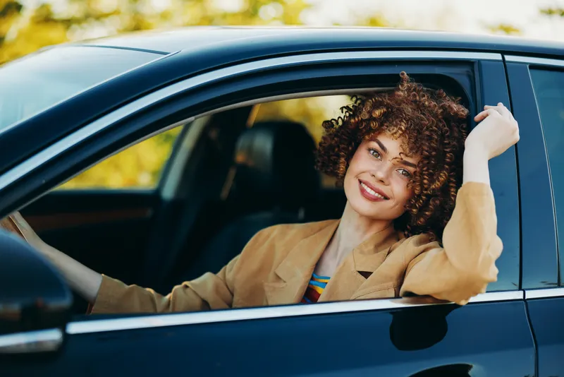 Smiling woman sits in a car window, capturing a casual lifestyle moment with retro film color tones, suggesting carefree urban commuting and everyday confidence.