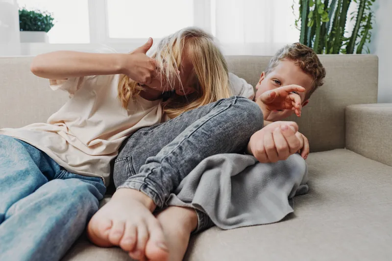 Young couple relaxing on sofa at home, playfully covering each other with hands and hair. Cozy atmosphere with casual clothing and natural light in modern living room.