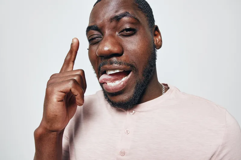 African American man with dark skin smiling and pointing finger up in casual shirt on white background. Positive expression, closeup portrait of confident young male.