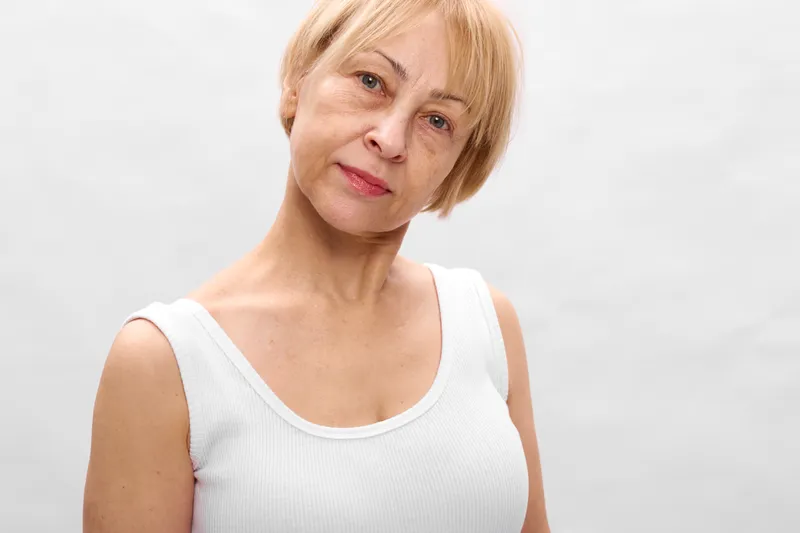 Woman portrait, blonde short hair, neutral expression, studio light, head and shoulders, soft focus, plain light background, calm mood, indoors