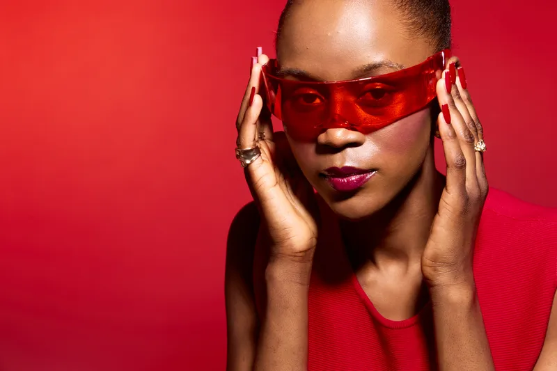 Close-up of a confident dark skinned African American woman wearing red sunglasses and matching red outfit against red background. Concept for fashion, style, and empowerment.