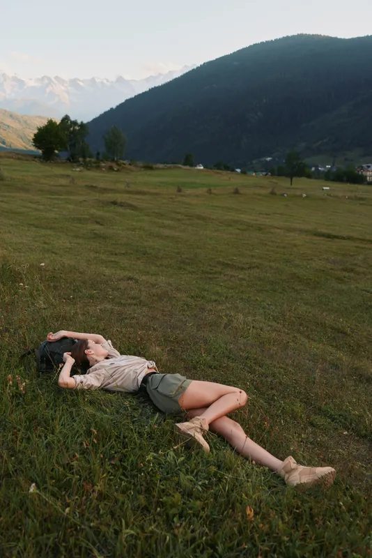 woman lifestyle outdoor meadow scene with a relaxed figure lying on grass, distant mountains and clear sky, showcasing connection with nature, leisure and peaceful wellness