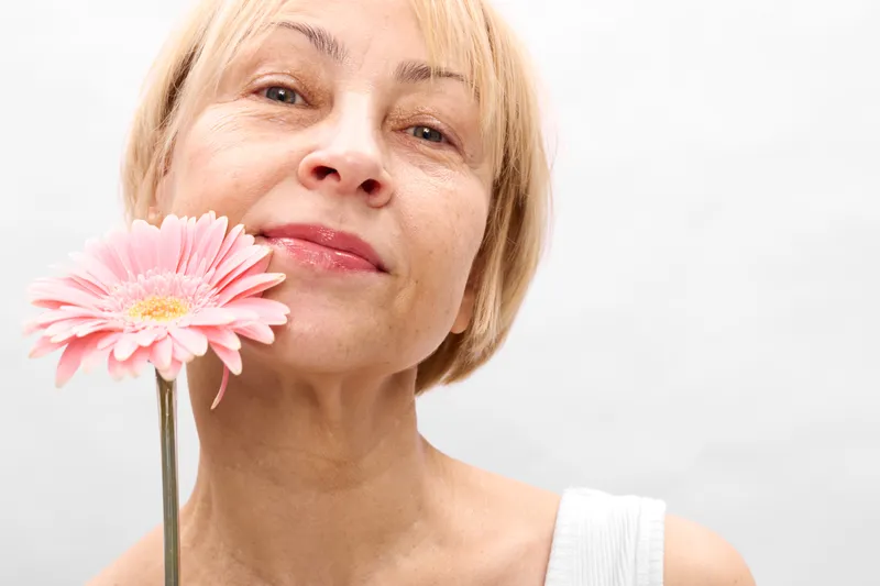 Woman, flower, closeup, spring, beauty, nature, portrait, blonde, female, holding a pink gerbera near her face, soft light on white background, gentle smile