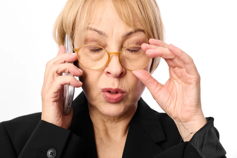 Elderly woman, phone to ear, glasses adjusting, studio white portrait, eyes closed, focused expression, calm pose, soft light, gentle makeup, relaxed posture, neutral background