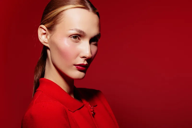 Portrait of a confident woman with slicked back hair wearing a red coat against a red background. The image highlights fashion, elegance, and bold color contrast.
