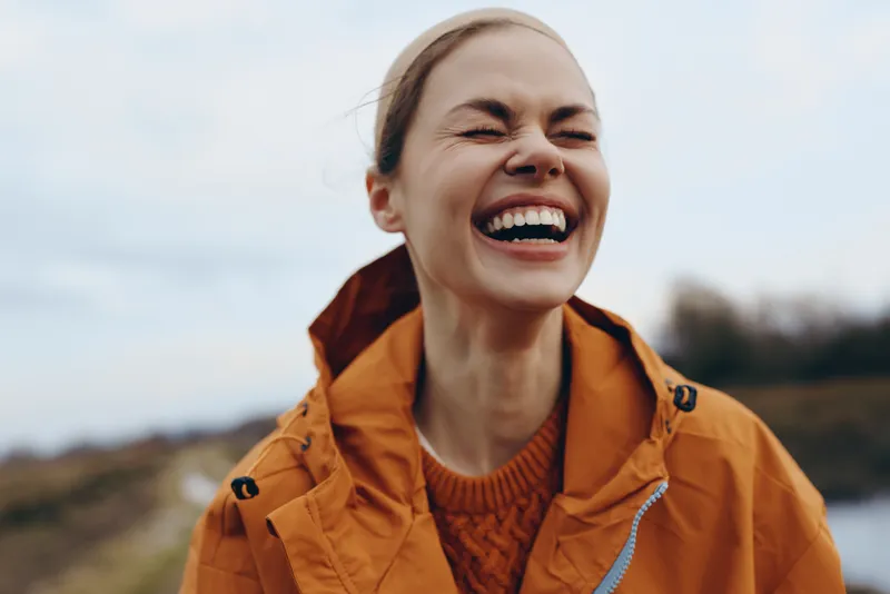 Woman lifestyle outdoor laughing smile jacket nature sky landscape, young woman in orange coat, cheerful face laughing, cloudy sky and countryside landscape, daylight outdoor walk, relaxed leisure