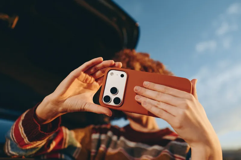Woman lifestyle holding smartphone for selfie, hands close up outdoors, warm sunset light and blue sky behind, casual striped blouse, photography moment, technology for daily connection, smile