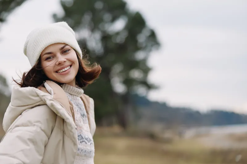 Woman outdoors winter portrait smiling coat beanie, portrait in a natural landscape with soft light, winter mood, casual fashion and cheerful expression for lifestyle photography and outdoor charm