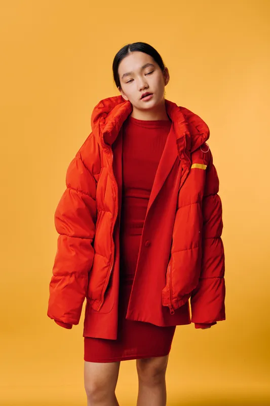Woman wearing red dress and oversized red jacket with closed eyes standing against orange background, fashion portrait, casual style with autumn or winter clothing, young adult.