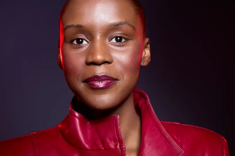Close-up portrait of confident dark skinned African woman with short hair wearing red leather jacket against dark background. Concept of beauty, fashion, empowerment, and style.