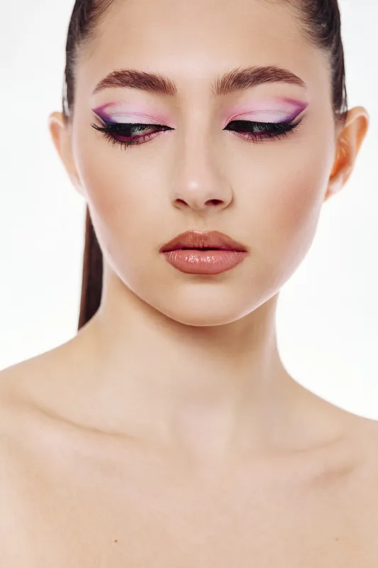 Young woman with creative fashionable purple and pink eye makeup looks down on white background. Close-up beauty portrait for makeup, style, fashion concepts.