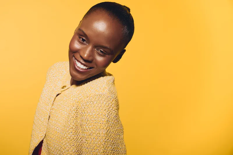 Smiling African woman with dark skin wearing a yellow knitted sweater poses against a bright yellow background. Concept for happiness, beauty, and positive emotions.