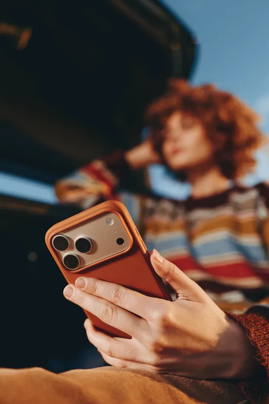 Woman lifestyle closeup, a hand holds a smartphone, a curly haired woman in a striped sweater is blurred in backseat light, bokeh suggests travel, casual photo taking